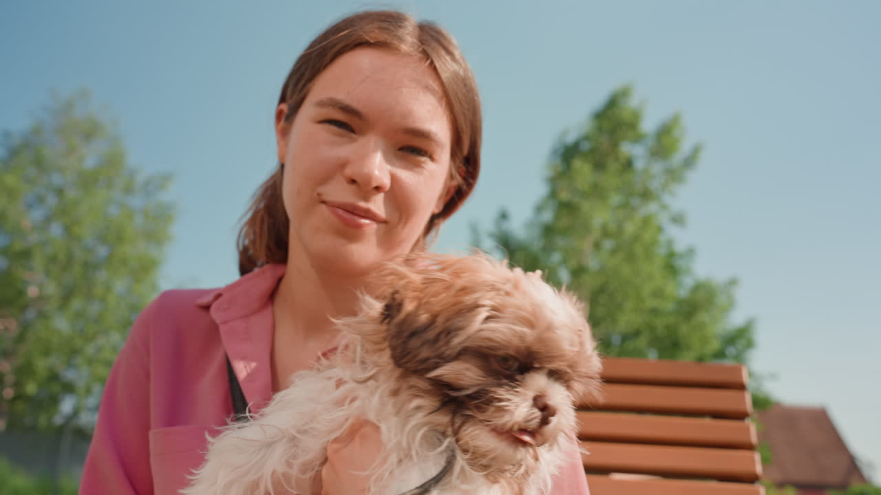 Joyful Woman Sitting With Her Little Dog Outdoors, Asian Woman Happily Posing With Her Tiny Dog On Park Bench, Sunlit Park Scene Featuring Woman And Her Small Dog Sharing Cheerful Moment