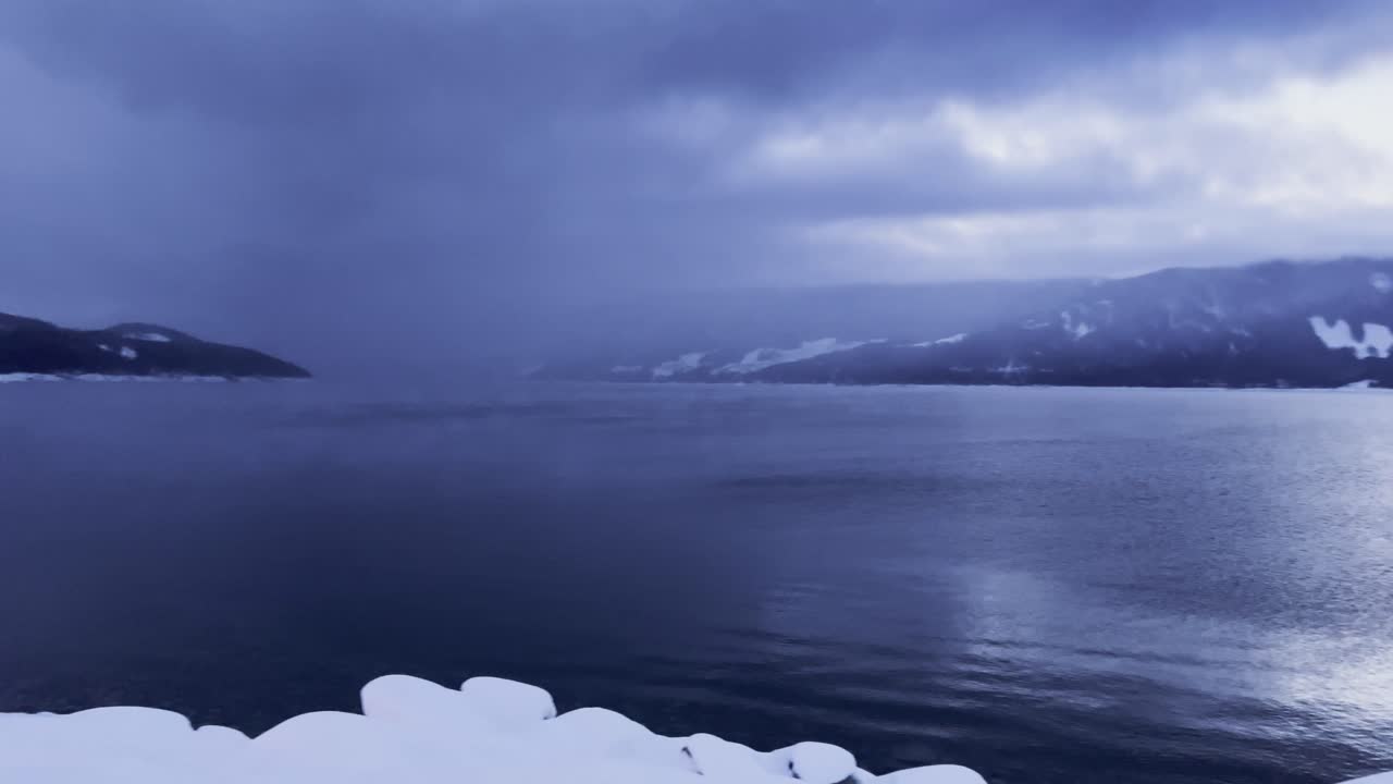 눈으로 뒤덮인 브리티시 컬럼비아의 극적인 어둡고 변덕스러운 위쪽 화살표 호수 위의 느린 팬과 페리 항구를 드러내는 것