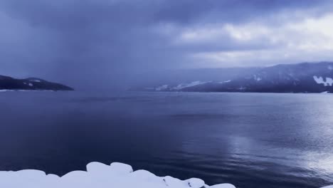 Langsamer-Schwenk-über-Den-Dramatischen,-Dunklen,-Stimmungsvollen-Upper-Arrow-Lake-British-Columbia,-Der-Mit-Schnee-Bedeckt-Ist-Und-Den-Fährhafen-Enthüllt