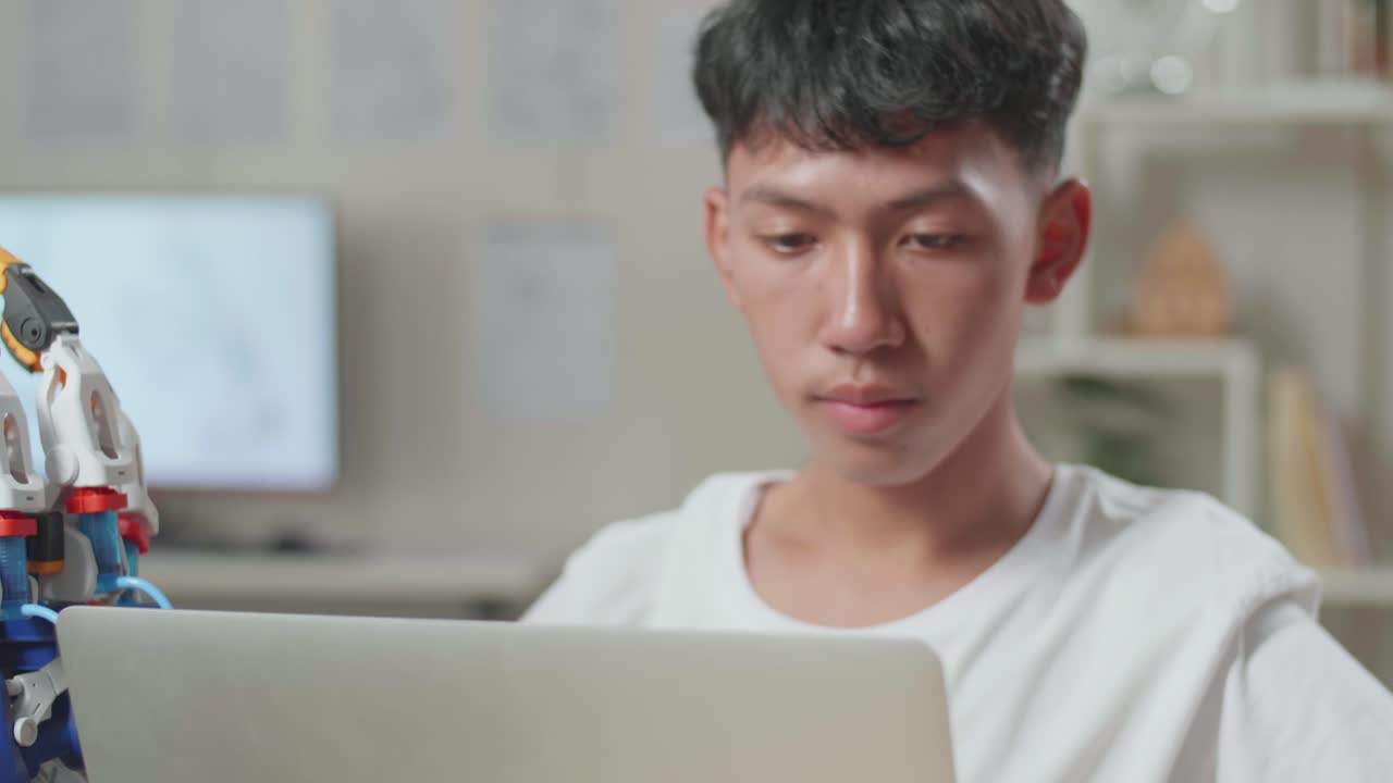 집에 있는 노트북에서 사이보그 손으로 작업하는 동안 두통을 고 있는 아시아 소년의 클로즈업