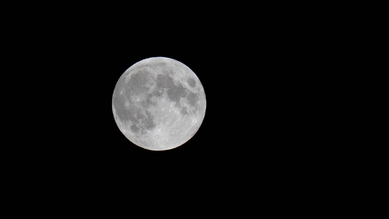 Lua cheia subindo lentamente no céu escuro, vista detalhada.