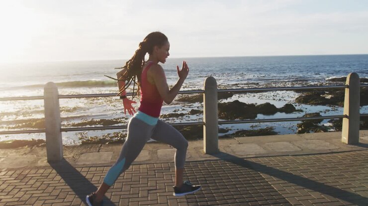 African american woman in sportswear running on promenade by the sea