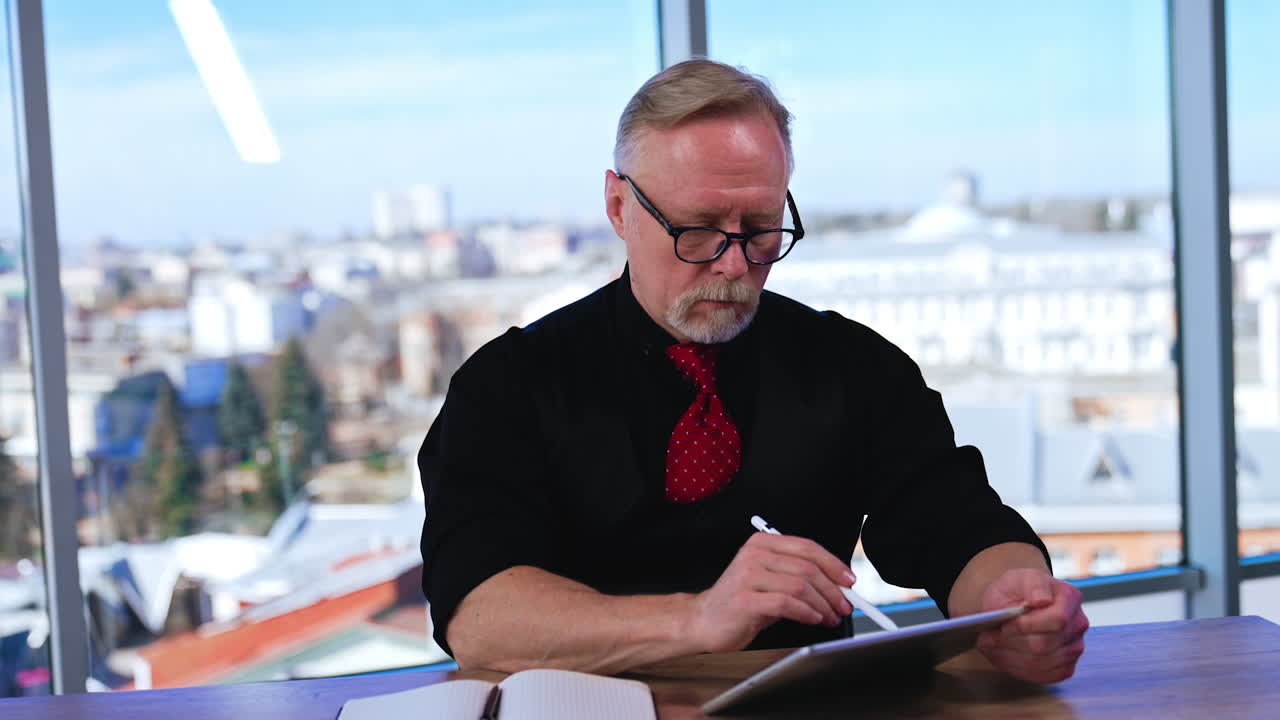 Productive busy man in black shirt and red tie sits at desk thinking. Businessman looks attentively at his I-pad in the office.