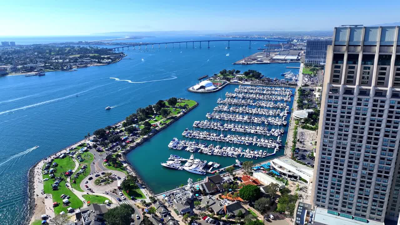 Veduta aerea del lungomare del centro di San Diego con il Manchester Grand Hyatt, l'Embarcadero Marina Park South, le imbarcazioni del porto turistico, il Rady Shell e il Coronado Bridge in una giornata luminosa e limpida.