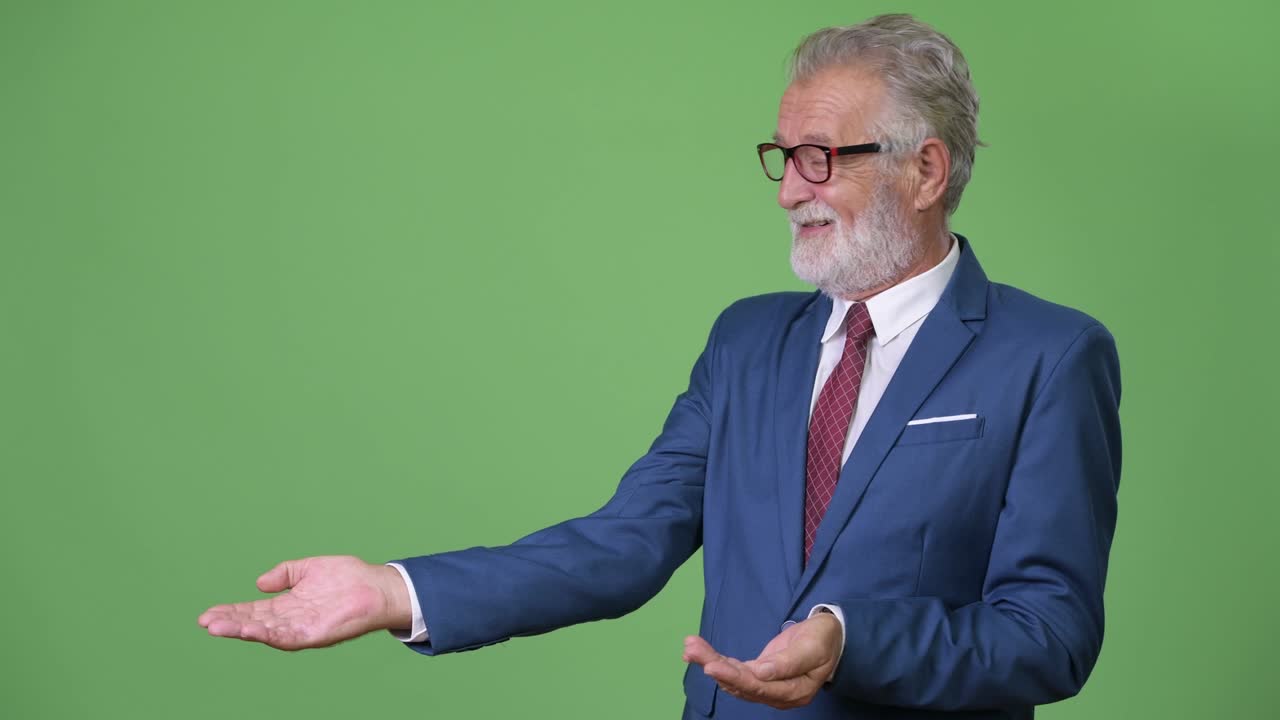 Handsome senior bearded businessman against green background