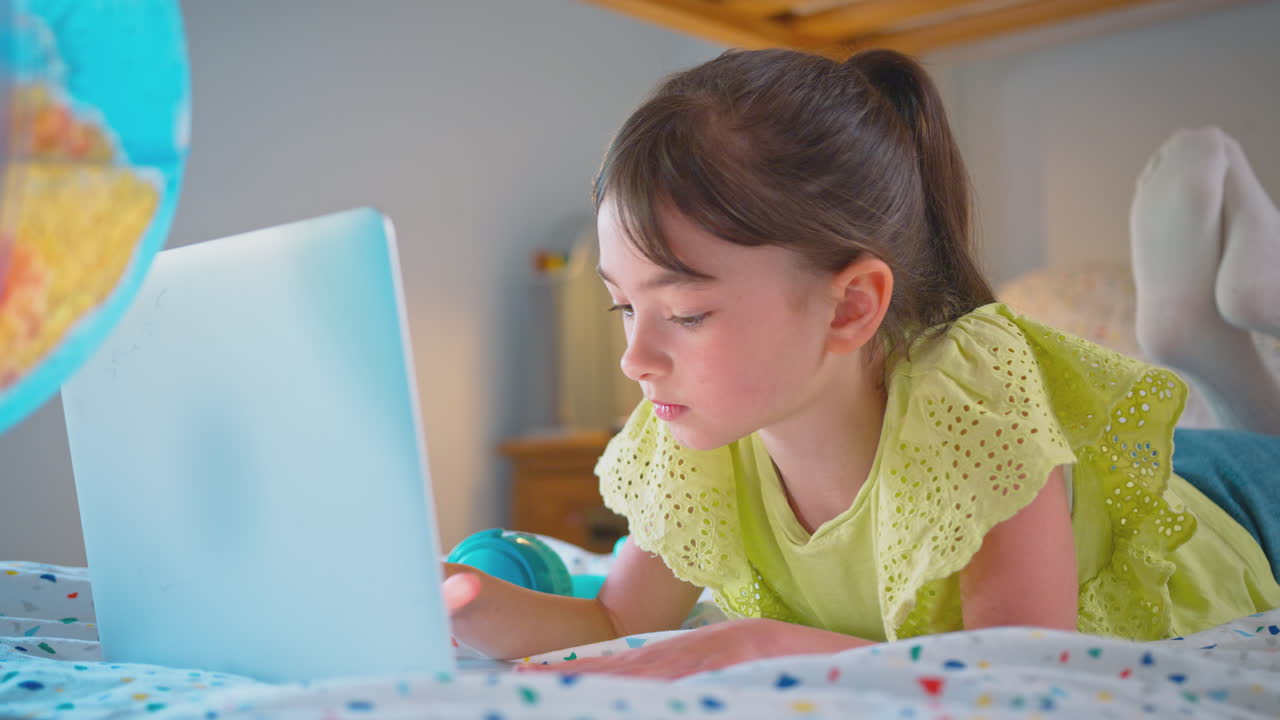 chica en el dormitorio acostada en la cama usando una computadora portátil con un globo iluminado