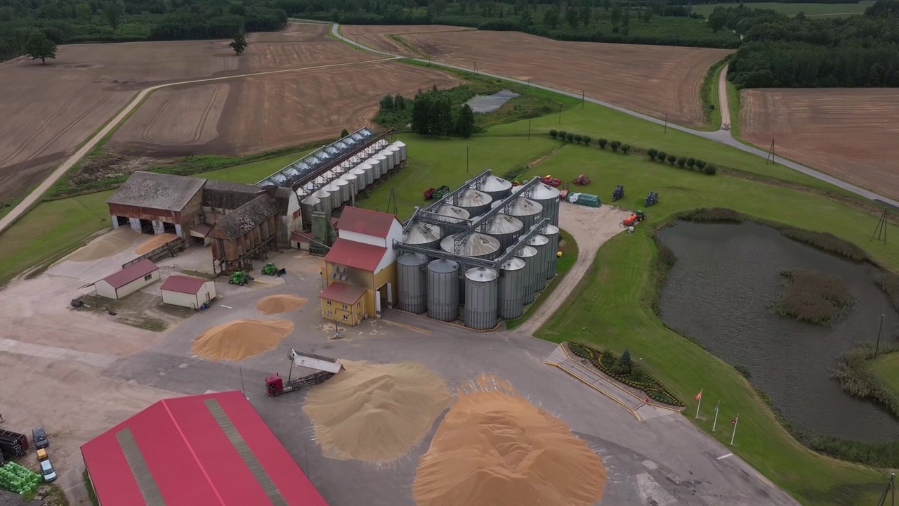 Imagens aéreas de drone de uma grande instalação agrícola de armazenamento de grãos com silos de grãos, edifícios de armazenamento, pilhas de grãos, máquinas agrícolas e campos circundantes na Letônia.