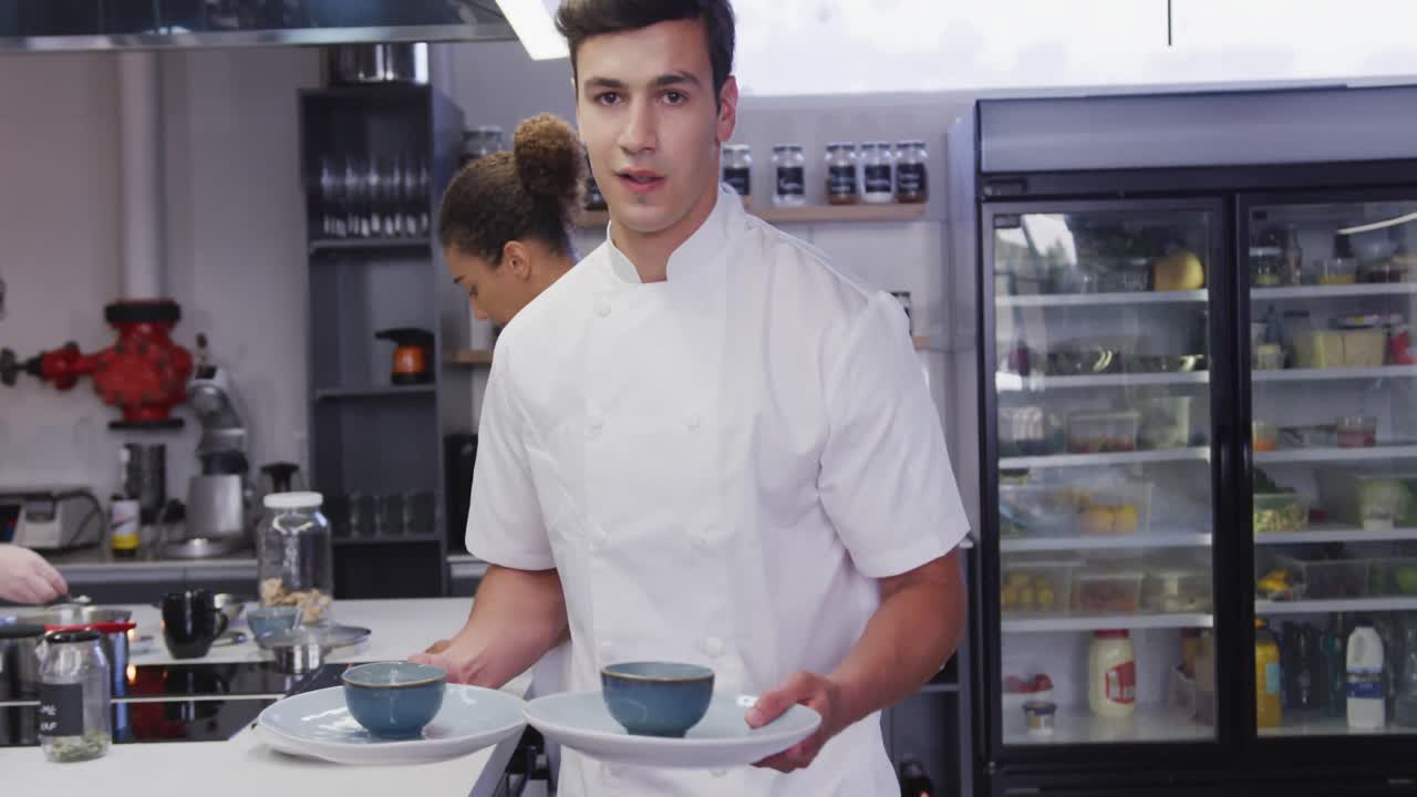 cocinero de raza mixta trabajando en la cocina de un restaurante, sosteniendo platos con comida, sonriendo a la cámara