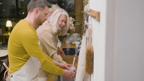 side view of a man washing the family dinner dishes at the sink in the kitchen while a mature woman helping him 2