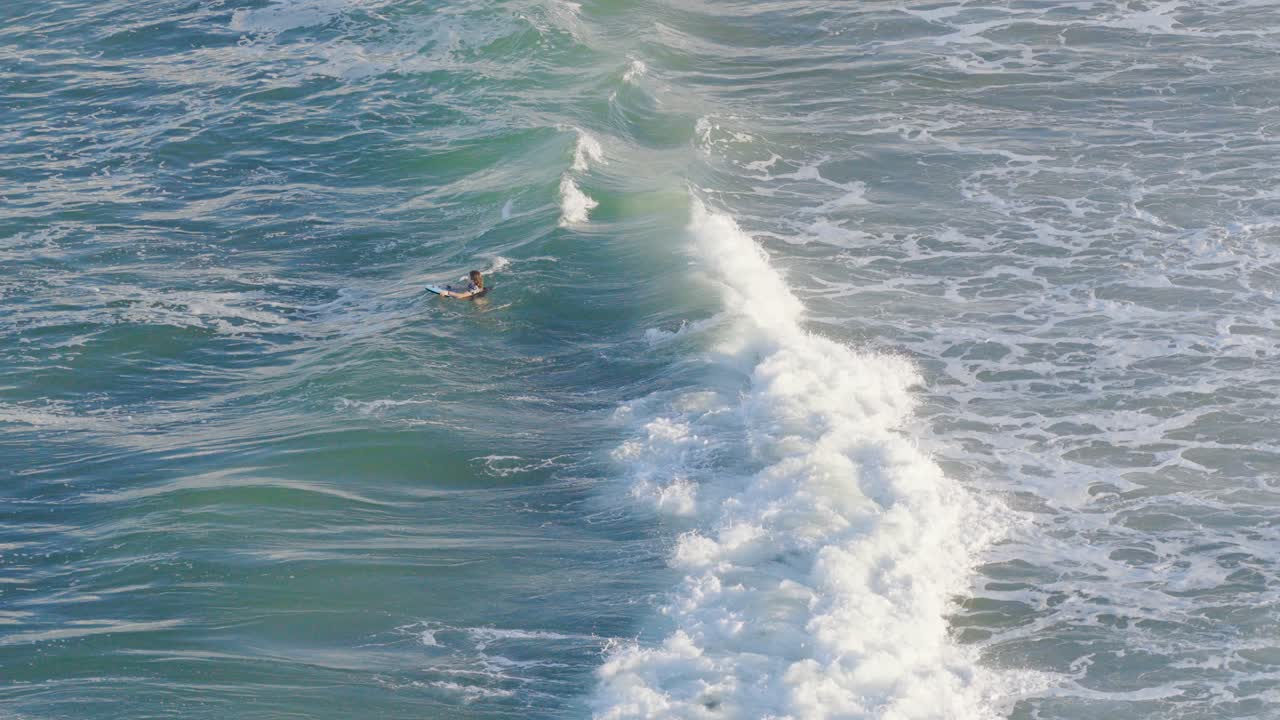 Two children enjoy playing in the ocean waves at Gold Coast, Australia, captured from a drone in bright daylight