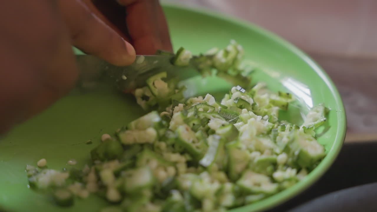 Closeup black hands dicing cucumber on green plate, instructional demo for mindful nutrition, portion control, low calorie salad, careful knife technique, calm pace, wellness focus, bright natural
