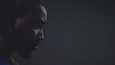 close up profile shot of male boxer or athlete training in gym preparing for fight or sports event against black studio background