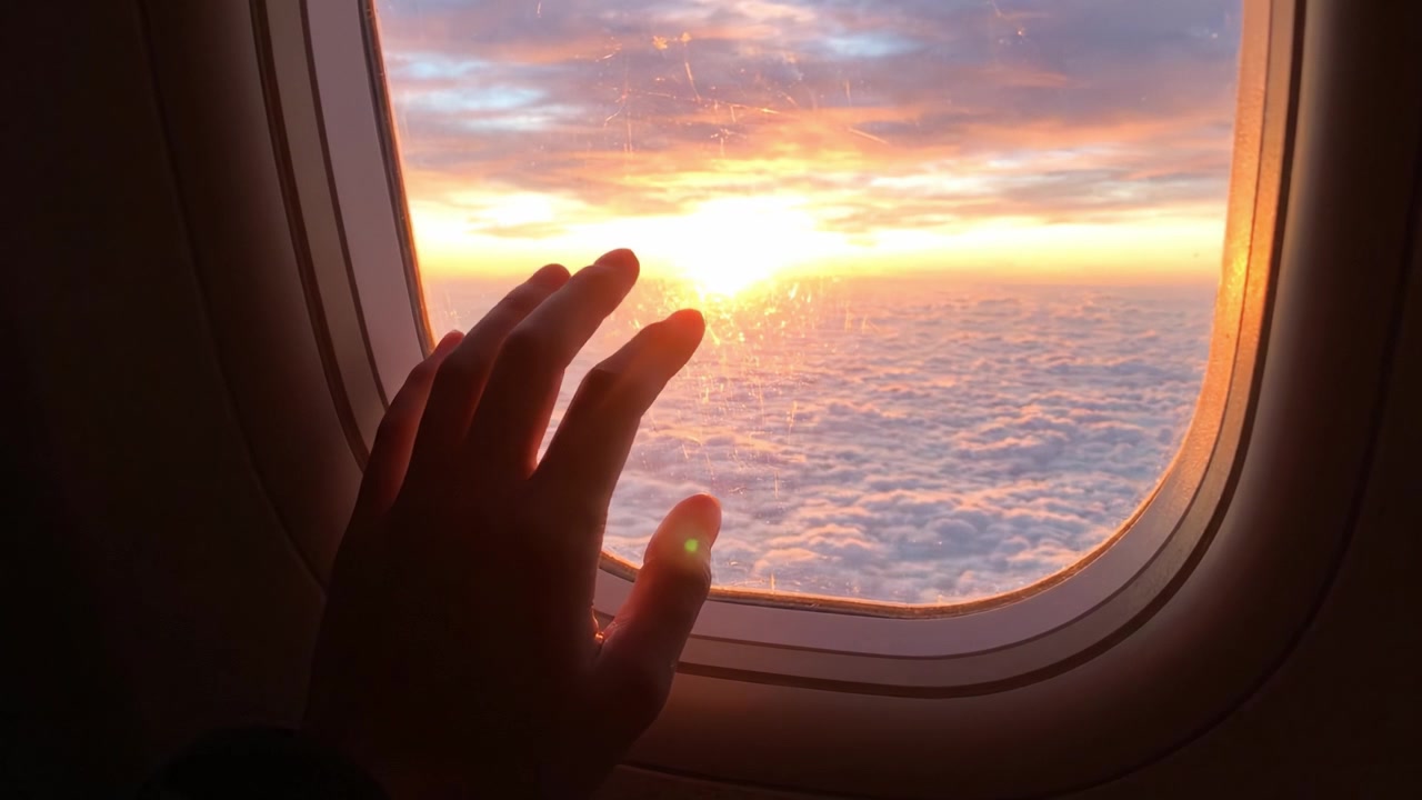 Capturing the Magical Moment of Sunset While Flying High Above the Clouds: A Serene Reflection Through an Airplane Window