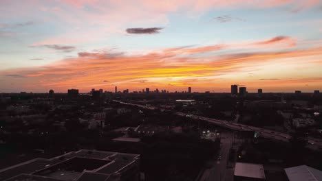 Vista-Aérea-De-Una-Autopista-Y-El-Paisaje-Urbano-Con-Silueta-De-Gran-Altura-En-Houston,-Cielo-Colorido-Del-Atardecer-En-Texas,-Ee