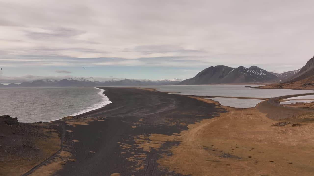 Aerial view of the dramatic Vestrahorn mountains and the Stokksnes peninsula in Iceland. Black sand dunes meet the sea under a dynamic sky.