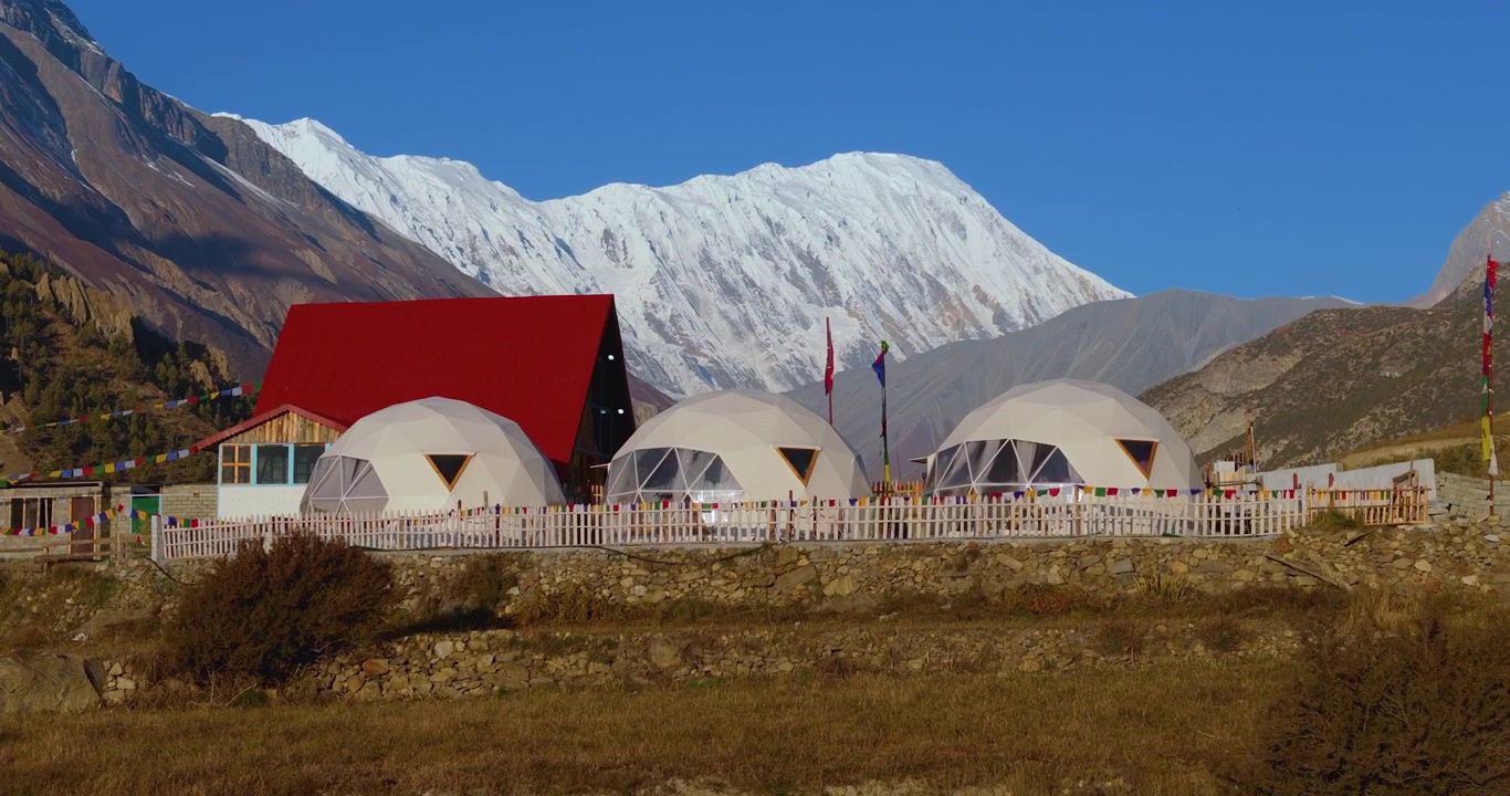 Annapurna Çevresi, Manang, Nepal'de, drone karla kaplı Himalaya dağlarının altındaki bir alp ana kampında glamping kubbe çadırlarını gösteriyor