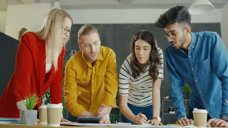 Grupo-De-Jóvenes-Empresarios-Multiculturales-En-La-Oficina-Trabajando-En-Una-Mesa-Grande-Mientras-Intercambian-Ideas-Sobre-La-Idea-De-Inicio