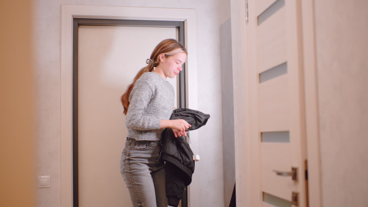 Young independent woman in gray sweater and jeans grabbing sweater and picking up keys while turning toward door, preparing to go out, showing casual lifestyle, confidence, and modern everyday