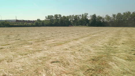 Drohnen-Flyover-Felder-Mit-Frisch-Geschnittenen-Heuballen-In-Richtung-Arbeitstraktor-Im-Sommer-In-Norditalien