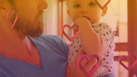 Animation-of-hearts-over-happy-caucasian-father-holding-baby