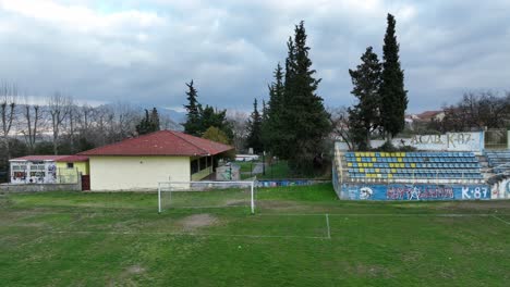 abandoned soccer field with a goal post, worn grass, and graffiti-covered bleachers