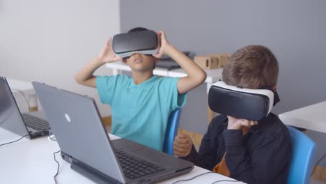 schoolboys wearing vr headset sitting at desk with laptop