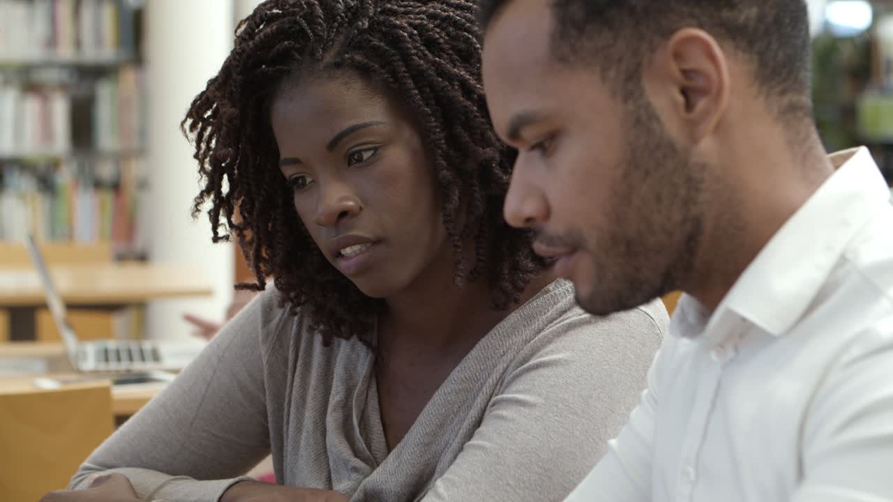 Focused colleagues sitting at library and communicating