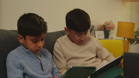 two young boys sitting on sofa at home playing games or streaming onto digital tablets 5