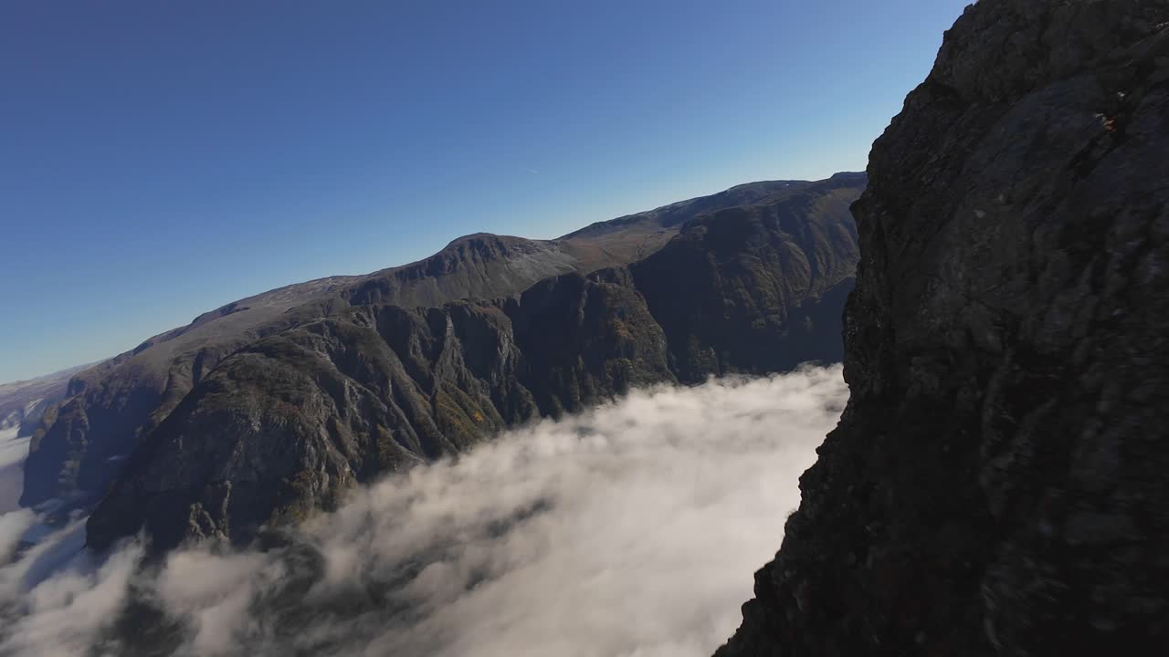 Fast FPV drone flies close to the ground around Bakkanosi, passing the cliff and people, revealing a magnificent panoramic view from the top