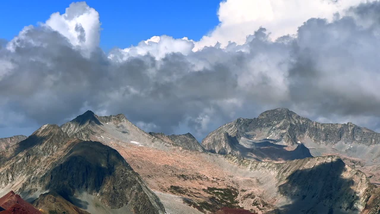 Capitol Peak Mount Snowmass summer weather aerial drone view Maroon Peak Maroon Bells Wilderness hiking fourteener Colorado Elk Range Rocky Mountains rugged terrain blue sky sun cloudy zoom out