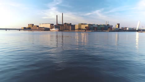 Low-tracking-aerial-shot-over-water-moving-towards-Ruoholahti,-Helsinki