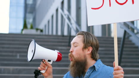 close-up view of bearded caucasian man talking on a loudspeaker and holding stop" signboard in the street"