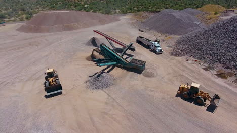 wide drone shot of an excavators loading rocks on a conveyer belt in a rock quarry