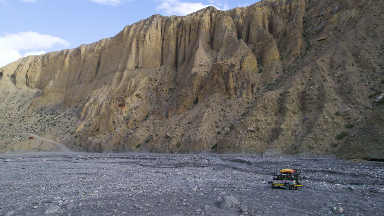 tomada de drone de un jeep de safari que viaja a través de la carretera del río en mustang, nepal
