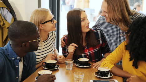 close-up view of multiethnic group of friends talking and laughing sitting at a table in a cafe