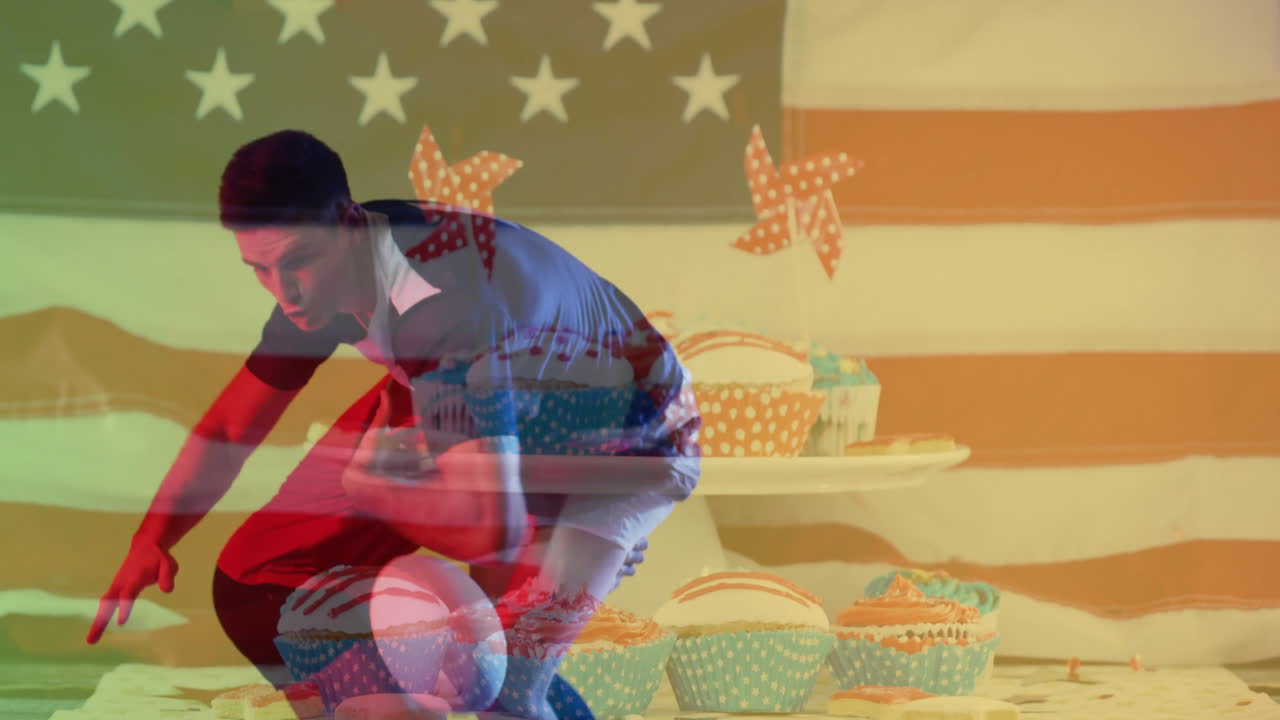 Crouching over cupcakes, man with American flag and pinwheels in background