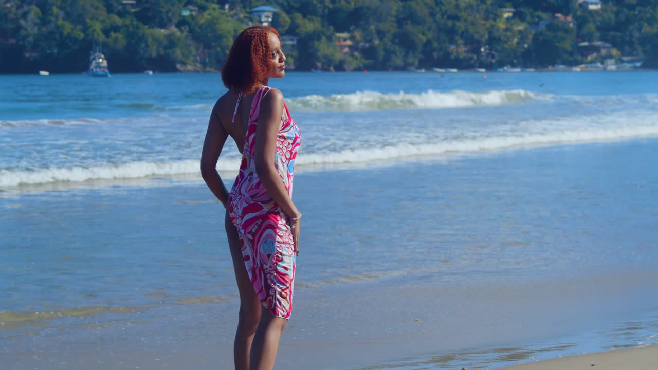 Ein Mädchen in einem Neon-Bikini steht knietief im karibischen Meer und blickt zurück auf den üppigen grünen Dschungel, der die tropische Küste säumt.