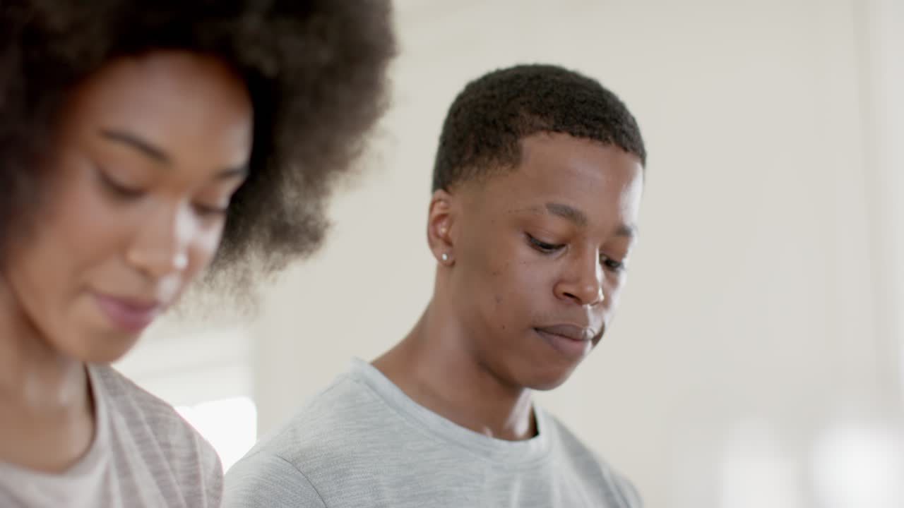 African American couple standing at kitchen counter, man inspecting counter and woman tasting snack