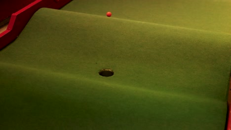 a golf ball rolls on a mini-golf course, illuminated by night lighting, approaching a hole on a sloped green