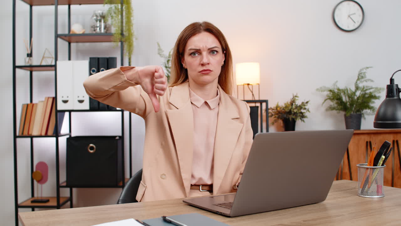 Una donna d'affari mostra il pollice verso il basso al laptop, gesto di disapprovazione, espressione infelice, reagisce a una recensione o risultato negativo