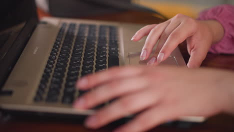 manos femeninas en vestido rosa sentadas en el centro comercial, trabajando con una computadora portátil, usando el touchpad y escribiendo, la escena se centra en la tarea a la mano con una elegante postura de escritura en un espacio público