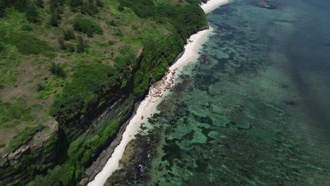 zoom in following tropical coastline with clear water and steep green cliffs, captured on a sunny day in ly son island