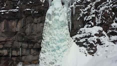 aerial view of frozen icy waterfall and snow capped cliff in mountain landscape, dolly drone shot