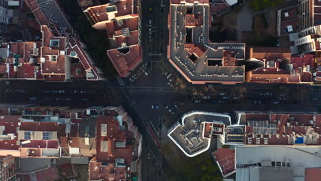 Birds-eye-shot-of-streets-and-buildings-in-urban-borough.-Cars-driving-on-streets-lined-by-parked-vehicles.-Barcelona,-Spain