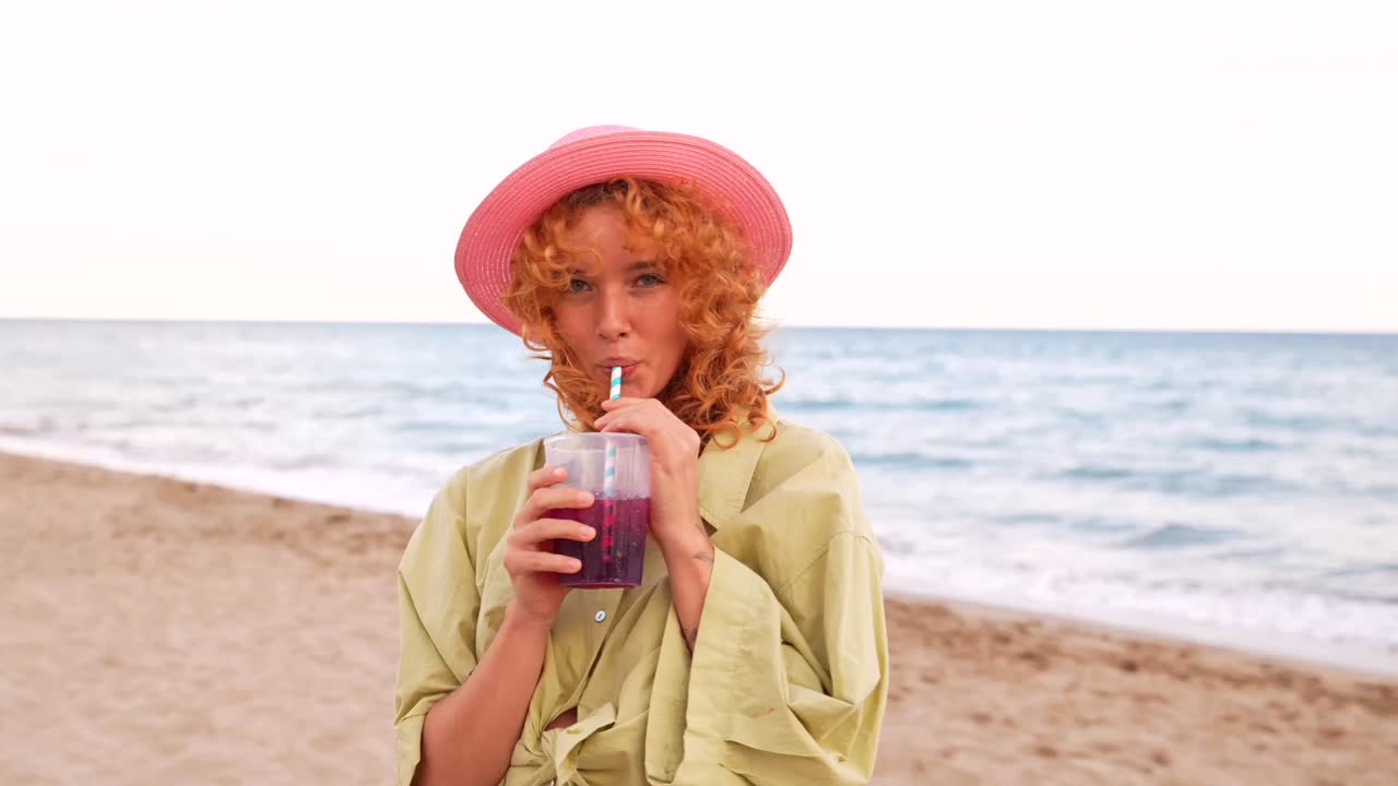 Woman with a pink hat enjoying a drink on the beach