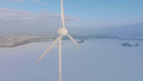 Vista-Aérea-De-La-Turbina-Eólica-Que-Genera-Energía-Renovable-En-El-Parque-Eólico,-Paisaje-Rural-Lleno-De-Nieve-Con-Niebla,-Tarde-Soleada-De-Invierno-Con-Luz-De-Hora-Dorada,-Amplio-Tiro-De-Drones-Moviéndose-Hacia-Atrás