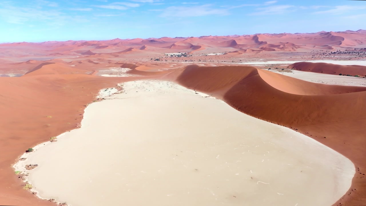 Vista de drone do famoso pan Deadvlei e suas árvores mortas abaixo das gigantes dunas vermelhas de Sossusvlei. As imponentes dunas vermelhas brilham contra as bacias de argila pálidas e rachadas desta antiga paisagem desértica