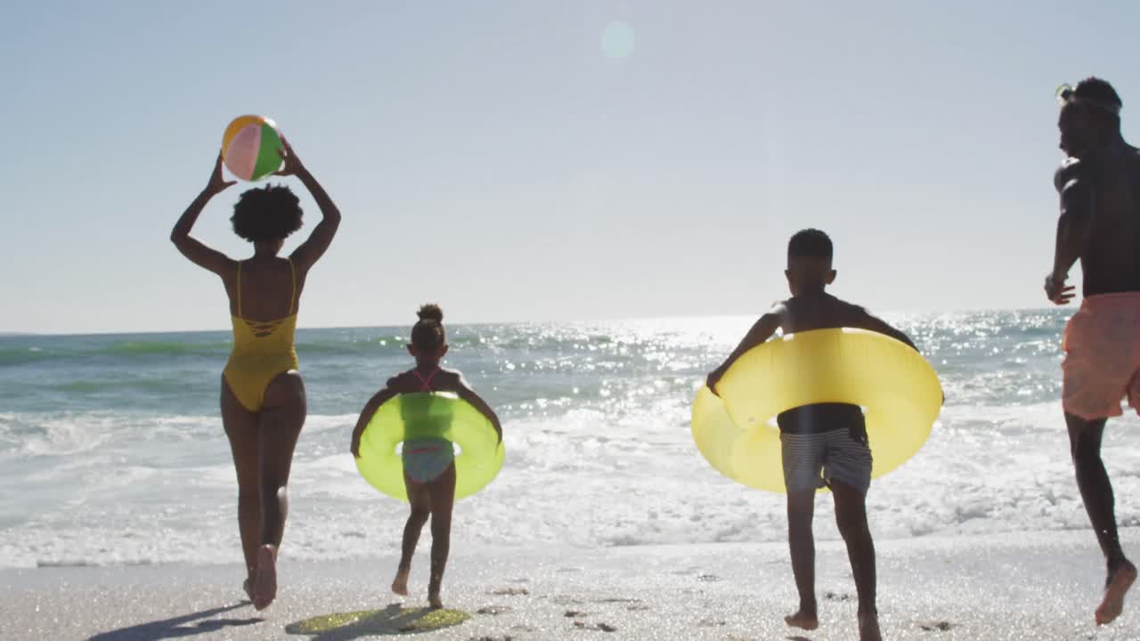 familia afroamericana con inflables corriendo hacia el agua en una playa soleada