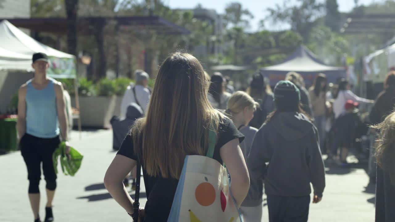 People walk through a bustling outdoor market on a sunny day