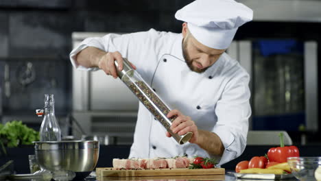 Männlicher-Koch-Pfeffert-Fleisch-In-Der-Küche.-Nahaufnahmekoch,-Der-Steak-Am-Arbeitsplatz-Pfeffert